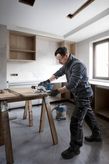 工事中のキッチンで、安全装備を身に着けた人が丸鋸で木材を切っています。