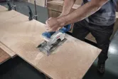 木工工場で人が丸鋸を使って合板を切っています。