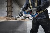 建設現場で安全装備を身に着けた人が丸鋸で木材を切っています。