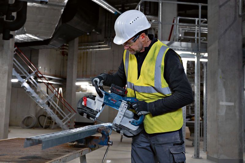 安全装置を装着した人がコードレスバンドソーで金属棒を切断しています。.