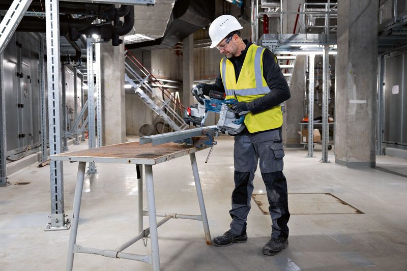 安全装置を装着した人がコードレスバンドソーで金属の梁を切断しています。.