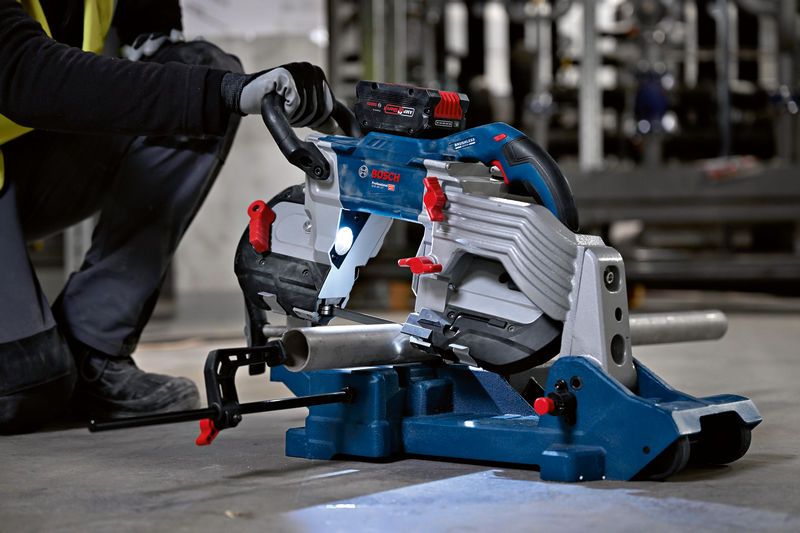 安全装置を装着した人が、取り付けられたバンドソーで金属パイプを切断します。.