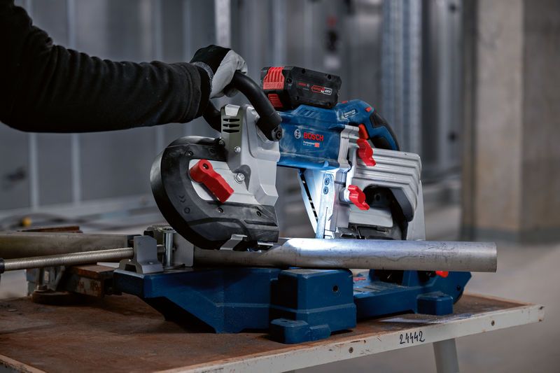 安全装置を装着した人がバンドソーを操作して金属パイプを切断しています。.