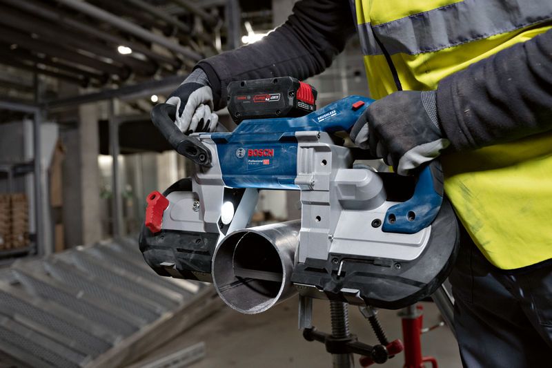 安全装置を装着した人がコードレスバンドソーを使用して金属パイプを切断しています。.