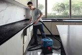 安全装備を身に着けた人が、湿式・乾式抽出機を使用してキッチンの引き出しを掃除しています。