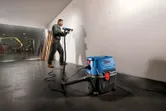 安全装備を身に着けた人が壁にドリルで穴を開けており、近くには乾湿両用抽出装置が接続されています。