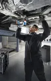 安全装置を装着した人がリフトされた車両の下でコードレスドリルを使用しています。