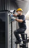 安全装備を身に着けた人が電動ドリルを使用して防犯カメラを設置しています。