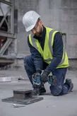 安全装備を身に着けた人がインパクトレンチで金属板上の大きなボルトを締めます。.