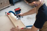 安全装置を装着した人がコードレスルーターを使用して木の板の縁取りをしています。