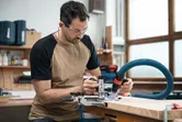 安全装備を身に着けた人が木の板の上でコードレスパームルーターを操作しています。.