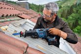安全装備を身に着けた人が、レシプロソーで屋根の上の木製の窓枠を切断しています。