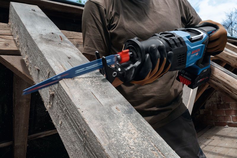 安全装置を装着した人が往復鋸を使用して木の梁を切断しています。.