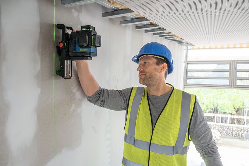 安全装置を装着した人がレーザーレベルツールを壁に合わせます。.