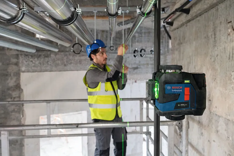 安全装置を装着した人がレーザーレベル測定ツールを使用してパイプの位置を調整します。.