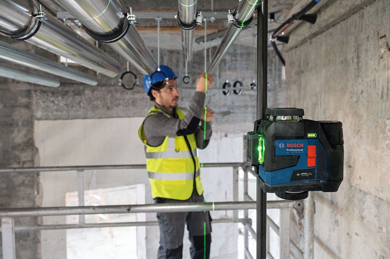 安全装置を装着した人がレーザーレベル測定ツールを使用してパイプの位置を調整します。.