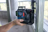 屋内で金属フレームに位置合わせされたレーザーレベルツールを持っている人。.