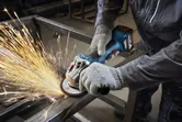 安全装置を装着した人がアングルグラインダーで金属の梁を研磨しています。