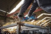 安全装置を装着した人がアングルグラインダーで金属の梁を研磨しています。.