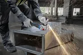 安全装備を身に着けた人が金属ダクトを研磨し、建設現場で火花を発生させています。