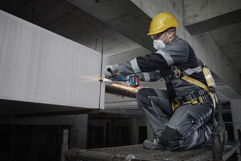 建設現場で、安全装備を身に着けた人が電動工具を使ってコンクリートを研磨しています。.