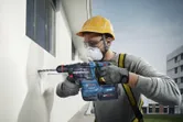 安全装備を身に着けた人が電動工具で外壁に穴を開けています。