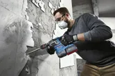 安全装置を装着した人が回転ハンマーを使用して壁からタイルを取り外します。.