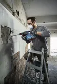 安全装備を身に着けた人が回転ハンマーで壁のタイルを取り外します。