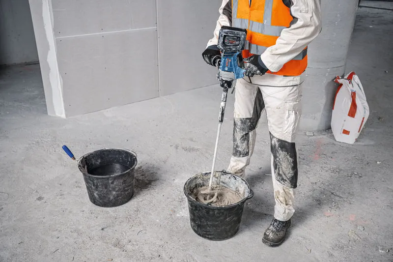 安全装備を身に着けた人が攪拌装置を使って建設資材を混ぜます。.