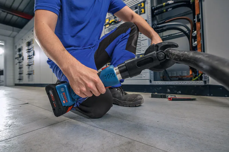 安全装置を装着した人が、太いケーブル上でコードレス油圧切断工具を使用しています。.