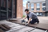 安全装置を装着した人がコードレスドリルを使用して屋外にデッキ板を設置しています。