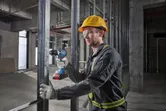 安全装備を身に着けた人が建設現場で金属フレームに穴を開けています。