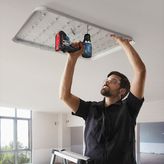 安全装置を装着した人が電動ドリルを使用して天井の照明器具を取り付けています。