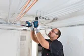 安全装置を装着した人が天井に穴を開けて電気配管を設置しています。