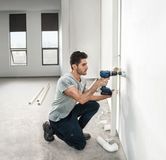 明るい未完成の部屋で、配管を設置するために壁に穴を開けている人。.