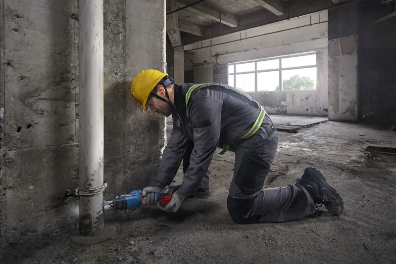 GSA 18V-24 安全装置を装着した人が、レシプロソーを使用してコンクリート壁の近くのパイプを切断しています。.