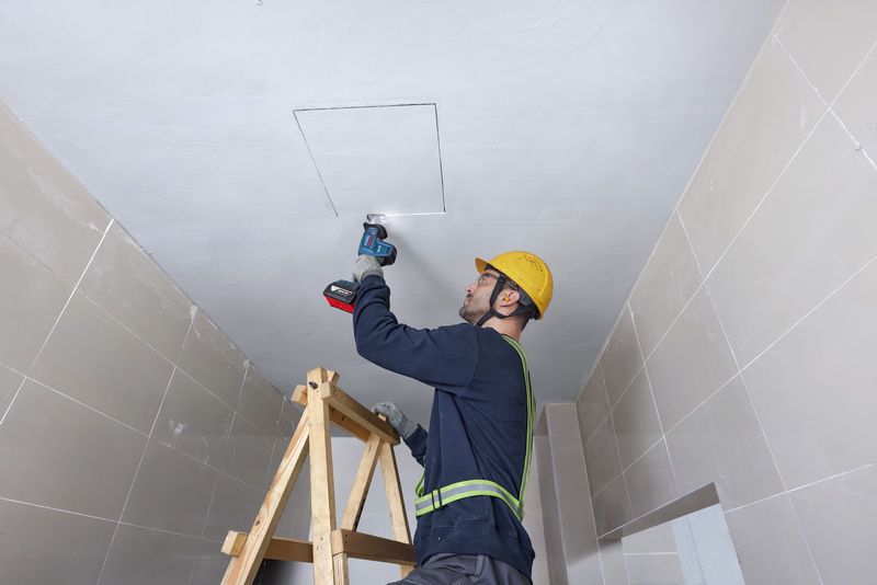 安全装置を装着した人がレシプロソーを使用して天井パネルを切断しています。.