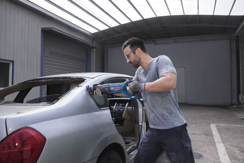 安全装備を身に着けた人がレシプロソーを使用して車の後部窓枠を切断しています。.