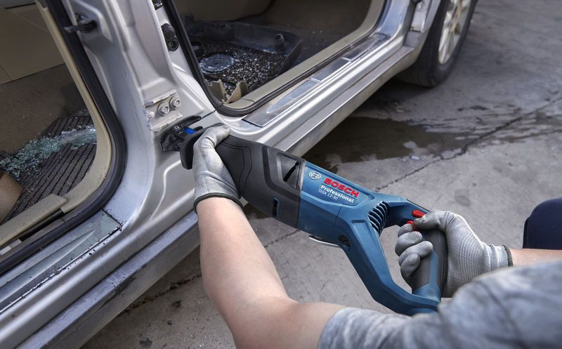 安全装置を装着した人がレシプロソーを使用して自動車のドア枠の金属を切断しています。.