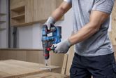 安全装置を装着した人が、コードレス回転ハンマーを使用して木材に穴を開けています。