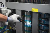 安全装置を装着した人が電圧テスターを使用して制御盤内の電気配線を点検しています。