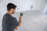 人が手持ち式サーモカメラを使用して、何もない部屋の床をスキャンしています。.