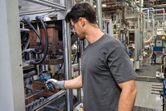 工場内で安全装備を身に着けた人がサーモカメラを使って機械を検査しています。.
