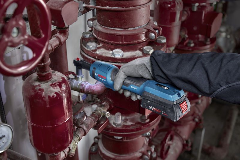 安全装置を装着した人が工業用配管にコードレスラチェットレンチを使用しています。.