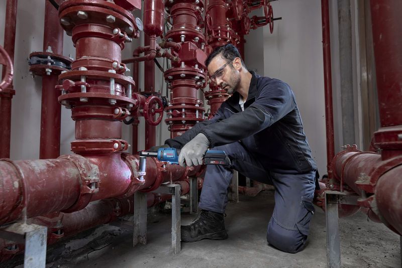 安全装置を装着した人が、赤い配管システムでコードレス ラチェットレンチを使用しています。.