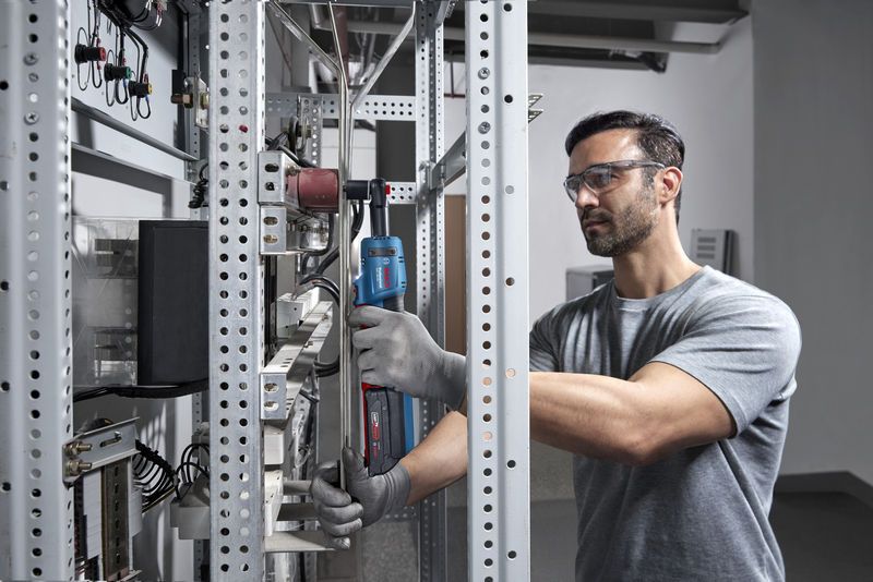 安全装置を装着した人が金属ラック上でコードレスラチェットレンチを使用しています。.