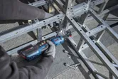 安全装置を装着した人が、コードレスラチェットレンチを使用して金属フレームのボルトを締めます。