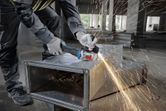 安全装備を身に着けた人がアングルグラインダーで金属ダクトを研磨し、火花を発生させます。