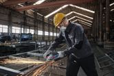 安全装備を身に着けた人が工場でアングルグラインダーを使って金属を研磨しています。