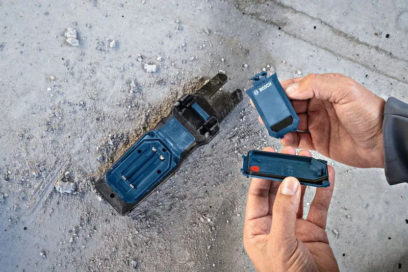 埃っぽいコンクリートの床の上で電動工具ベースのバッテリーを交換している人。.
